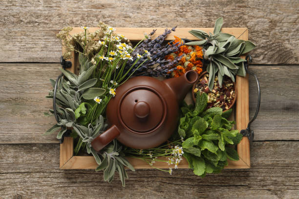 Assorted dried herbs and a ceramic teapot on a wooden table