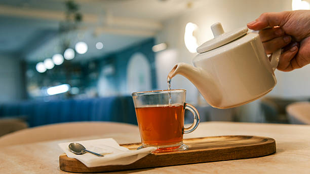 Pouring hot water into a glass teapot with visible herb infusion