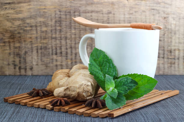 Fresh ginger root and peppermint leaves beside a teacup